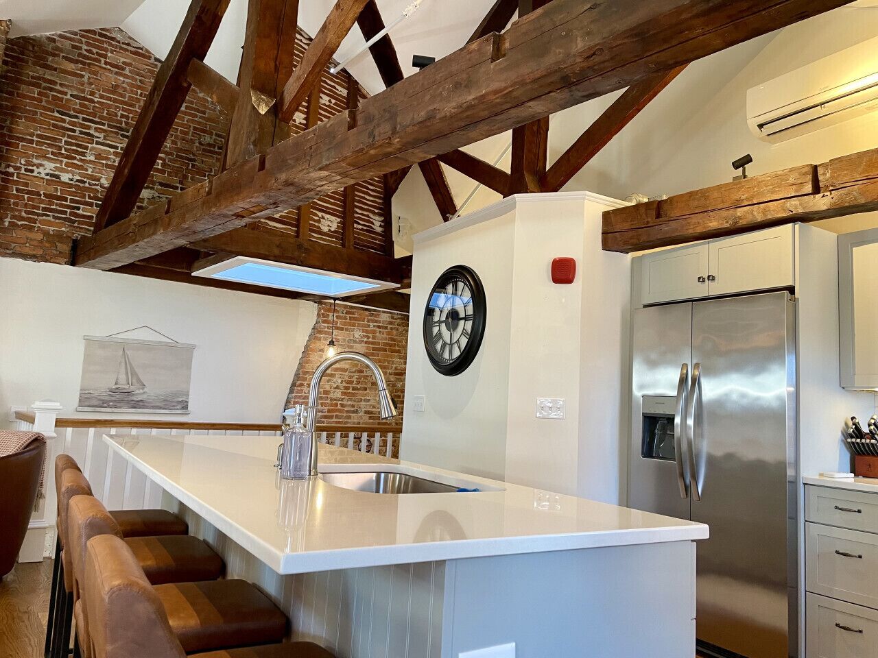 A modern kitchen with a central island, stainless steel appliances, and exposed wooden beams.
