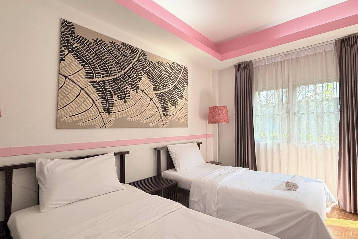 A hotel room with two beds, a large abstract painting, a floor lamp, and a window with curtains.