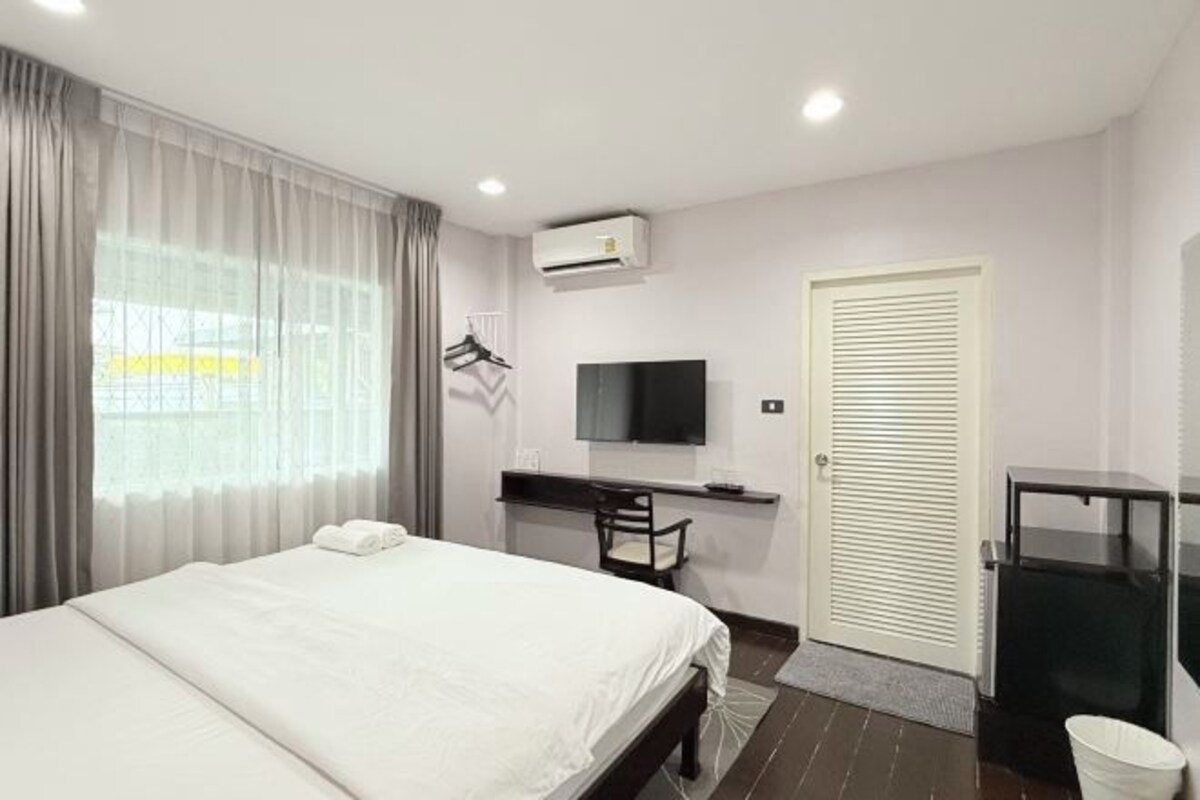 A hotel room with a bed, a desk, a television, and a door with a louvered design.