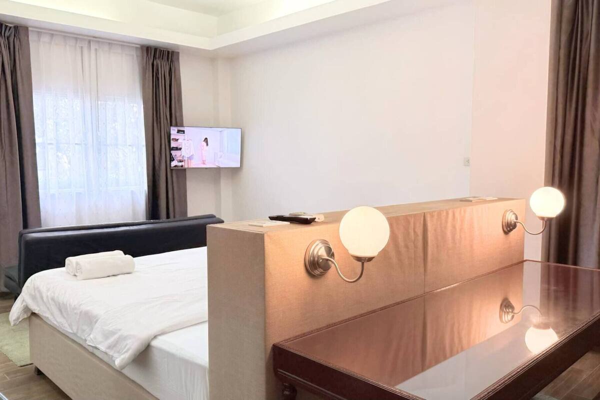 A hotel room with a bed, a desk with a computer, a TV on the wall, and curtains.