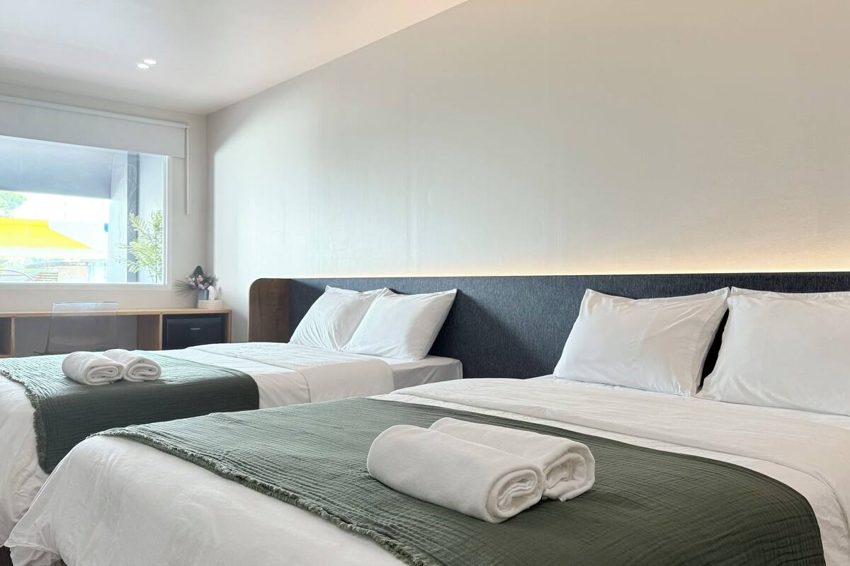 A hotel room with two beds, a desk, and a window with a view.