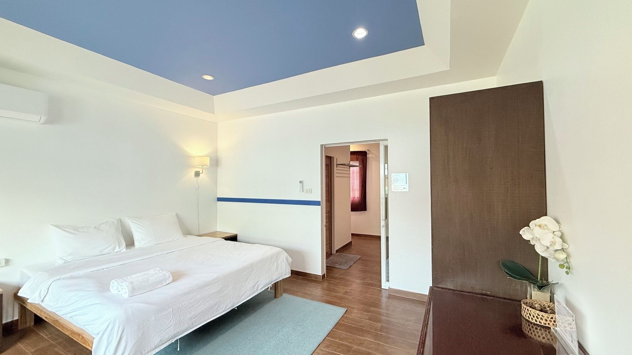 A modern hotel room with a large bed, a nightstand, a wall-mounted lamp, and a view of the hallway.