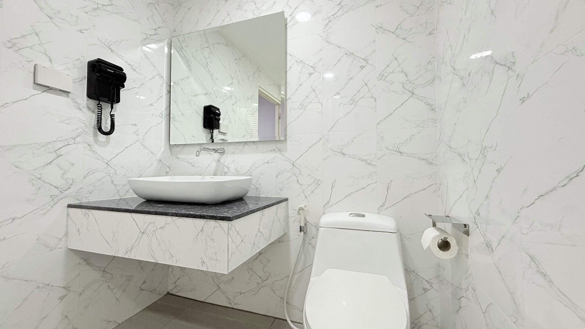 A bathroom with a white marble sink, a mirror, a black telephone, and a toilet.