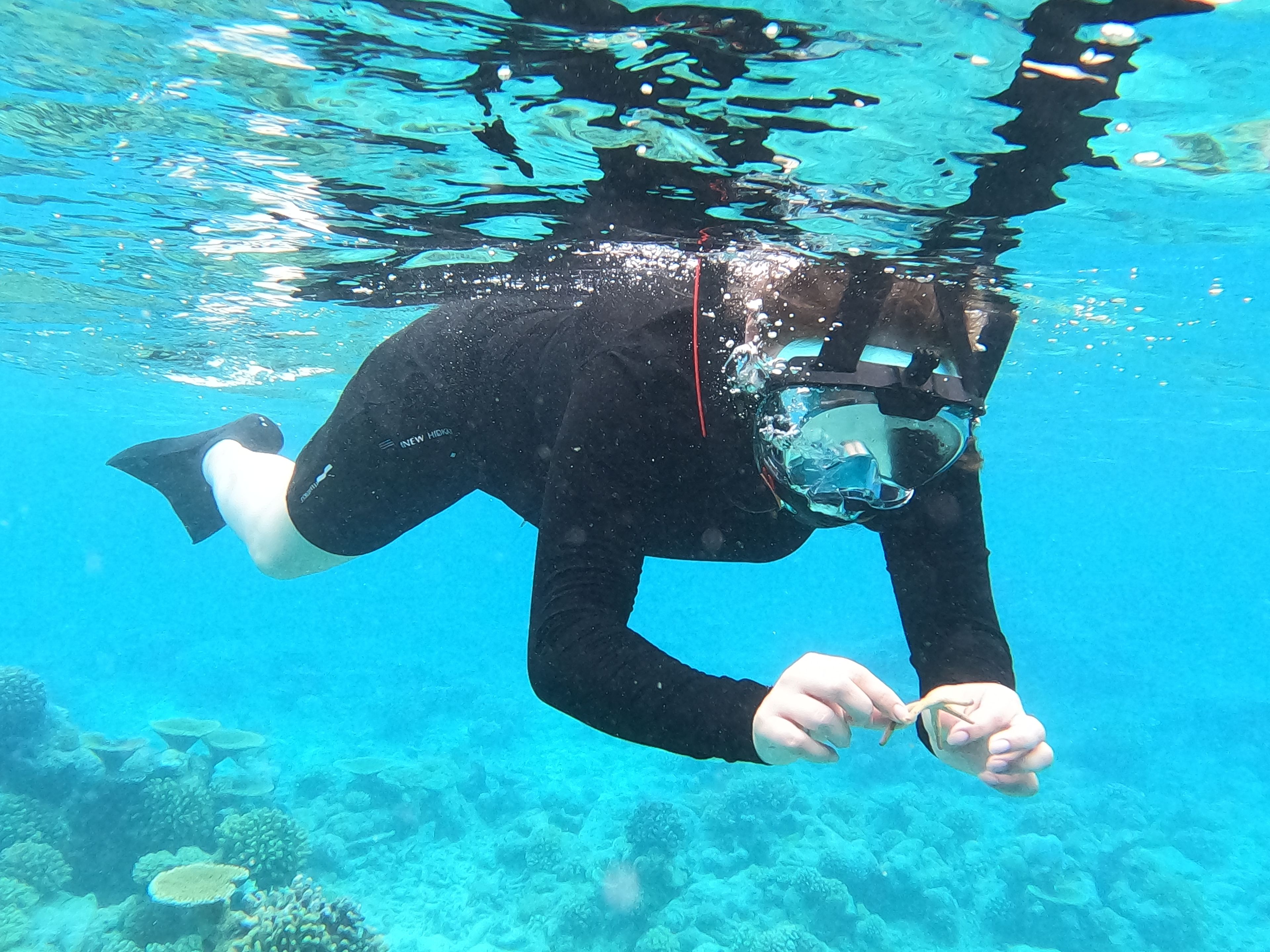 Une personne se trouve sous l’eau, dans un environnement clair et bleu, peut-être une piscine ou un espace aquatique aménagé.
