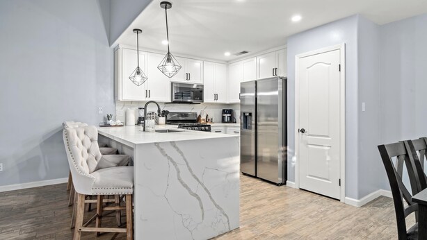 A modern kitchen with white cabinetry, a marble island, and stainless steel appliances.