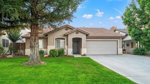 A residential house with a garage, a well-maintained lawn, and a large tree in the front yard.