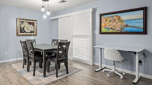 A dining area with a table and chairs, a white desk with a chair, and two framed artworks on the walls.