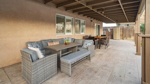 An outdoor patio with wicker furniture, including a sofa and a table with benches.