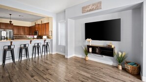 Una cocina moderna con armarios de madera, una isla central con taburetes de bar, un televisor de pantalla plana en la pared y un ventilador de techo.