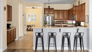 Una cocina moderna con armarios de madera, un refrigerador de acero inoxidable y una barra con taburetes.