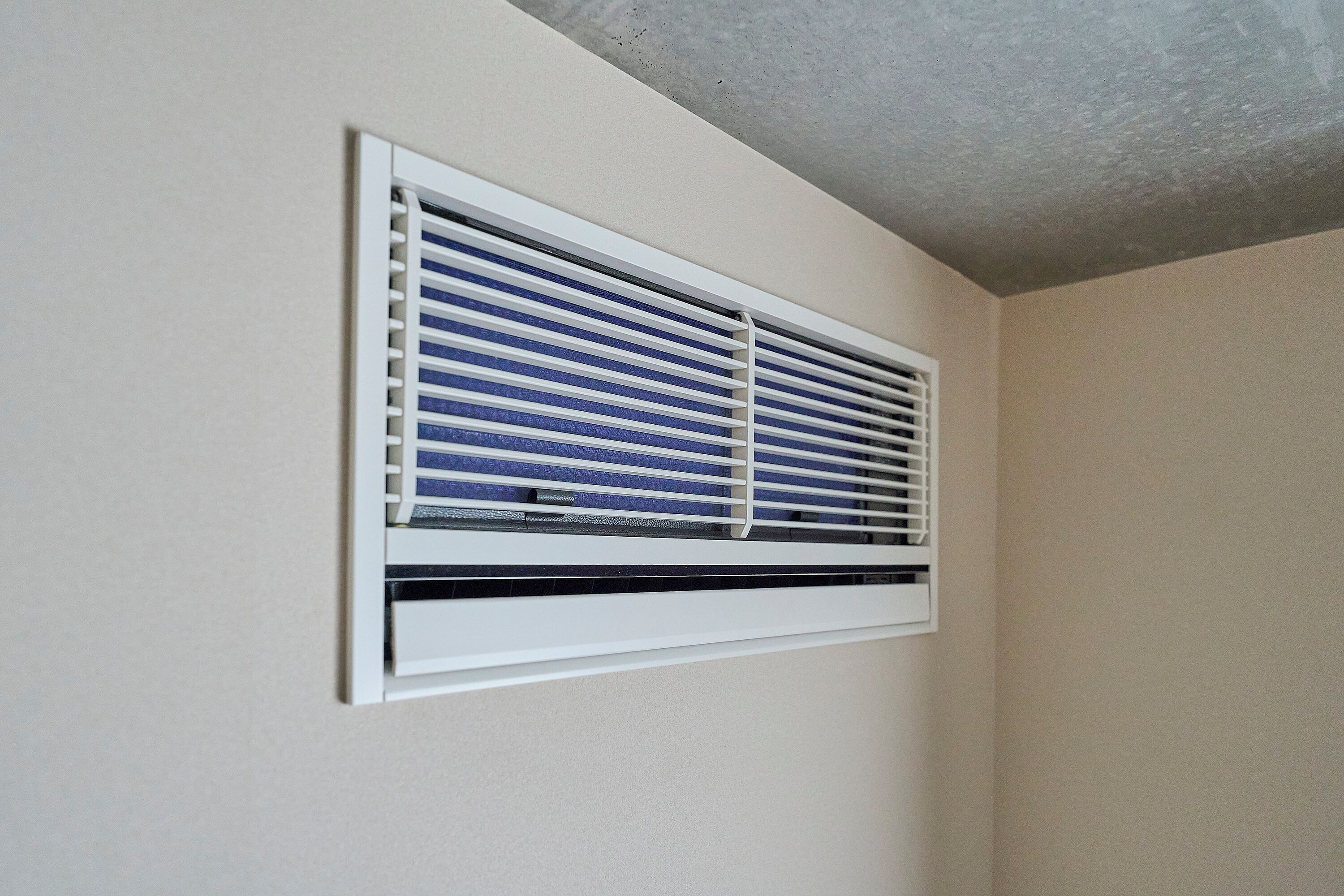 A window with horizontal blinds, a white frame, and a small air conditioning unit below the blinds.