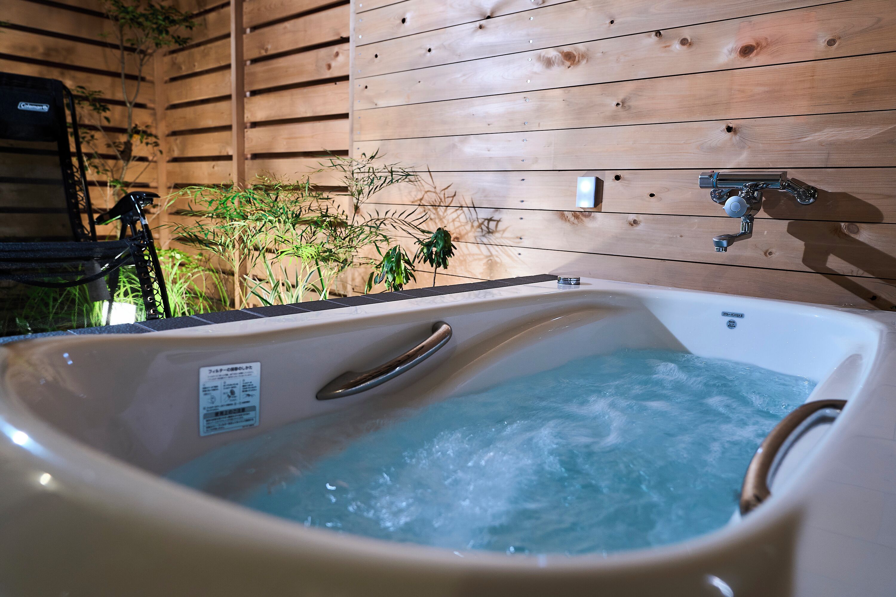 A hot tub with a wooden wall and a metal faucet.