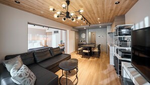 Un salon moderne avec un canapé en cuir noir, une table basse ronde et un coin repas doté d’un plafond en bois et d’étagères intégrées.