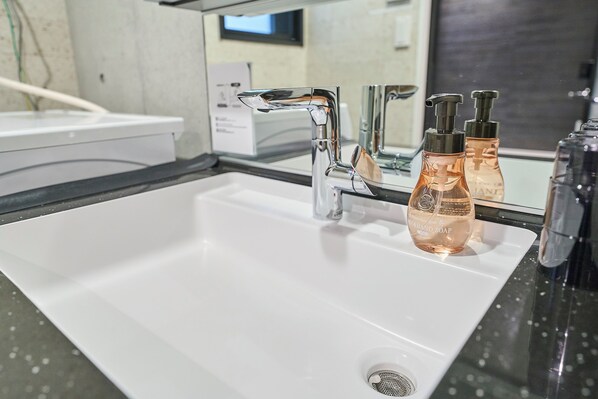 A modern bathroom with a white sink, chrome faucets, and two bottles of hand soap. - R.KAMAKURA (Kamakura)