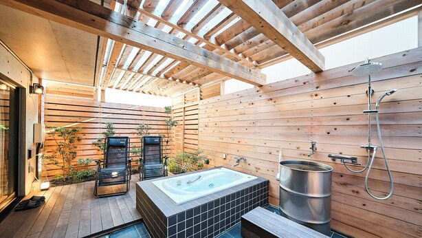 Une terrasse en bois avec un jacuzzi, un grand tonneau en métal et un banc en bois.