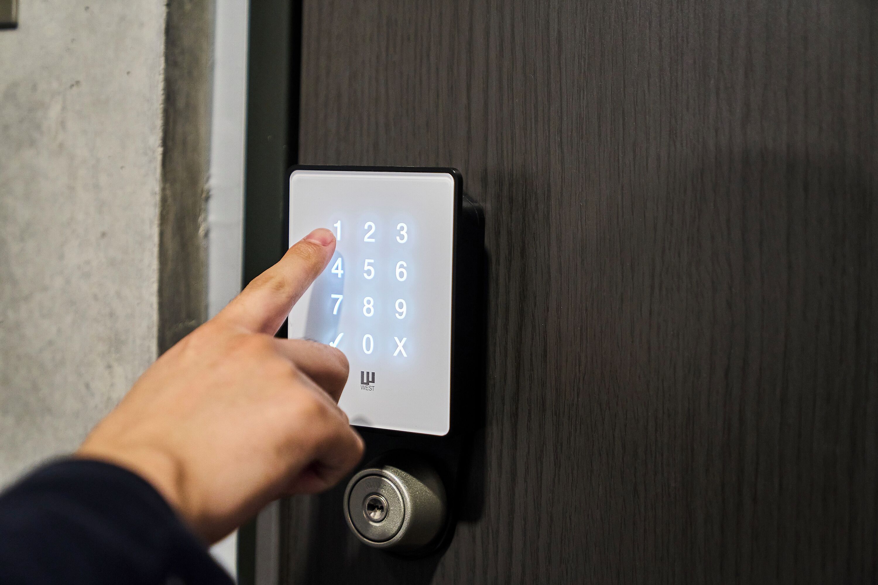 A hand pressing a numeric keypad on a door lock.