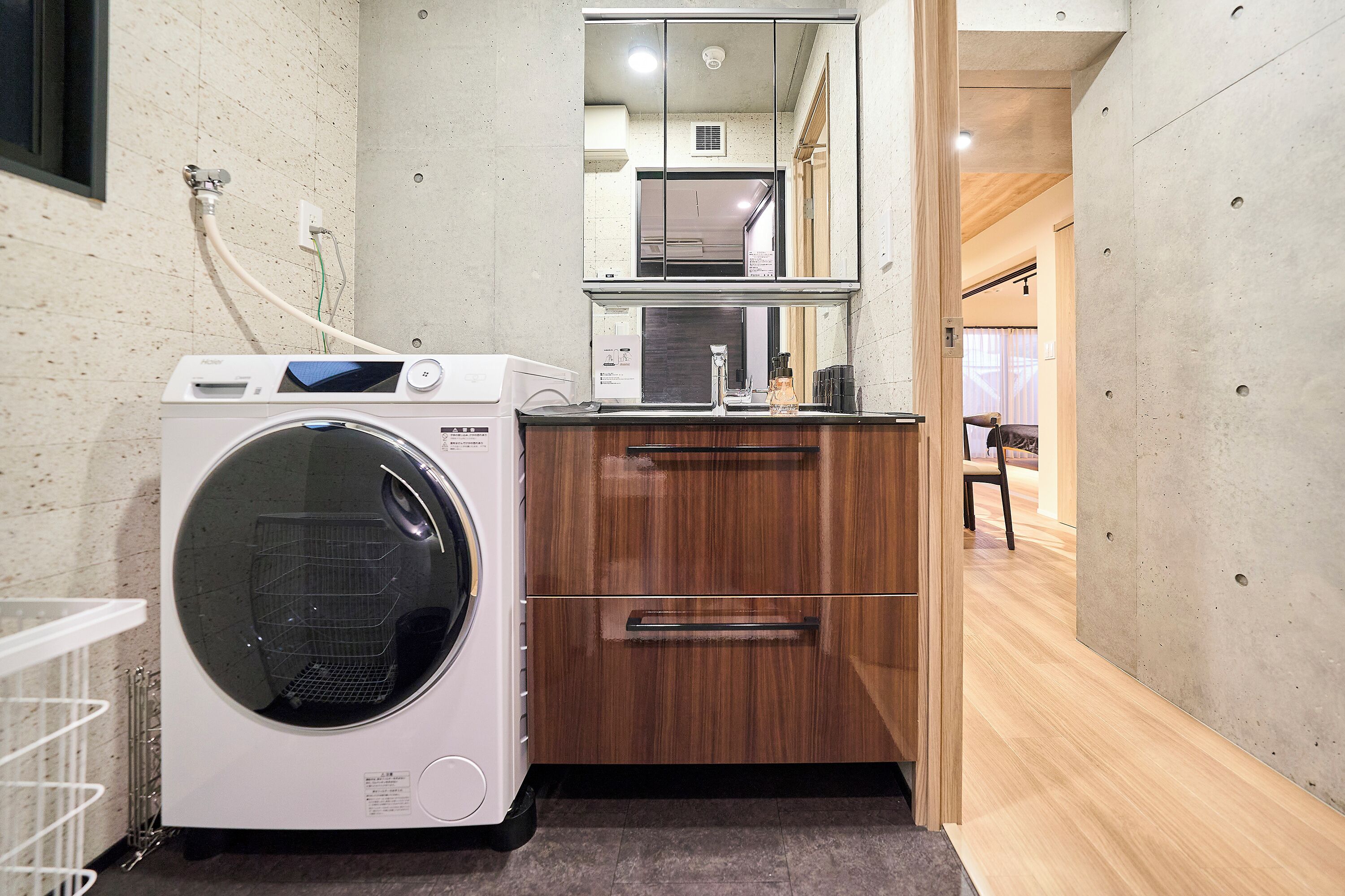 A compact laundry area with a washing machine, a wooden cabinet, and a mirror.