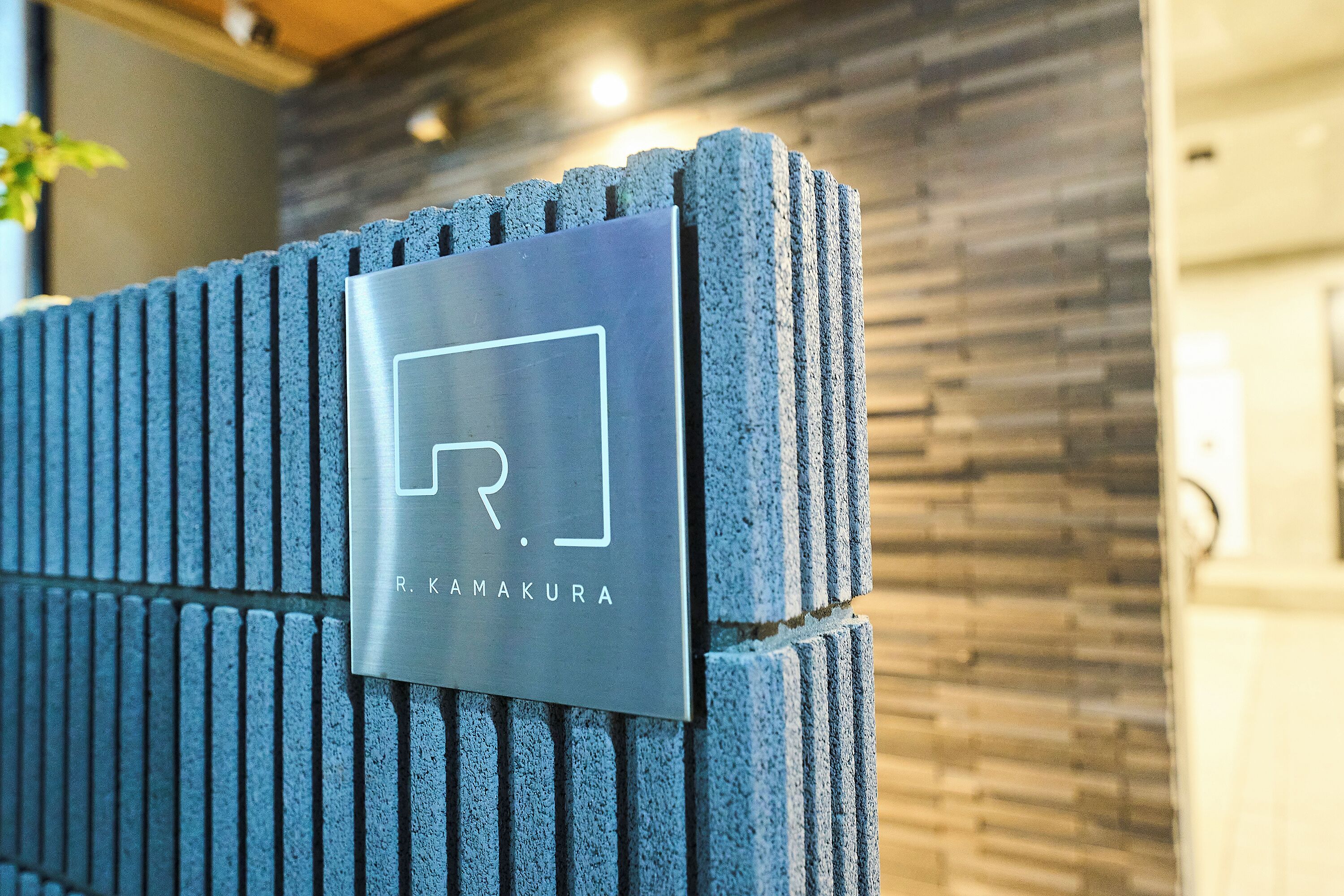 A metallic plaque with the text "R. KAMAKURA" on a textured wall.