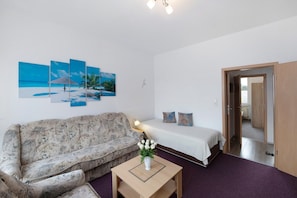 A room with a sofa, a bed, a small table with a vase, and a wall with three paintings. - Holiday Apartment 'Laage' with Wi-Fi (Laage)