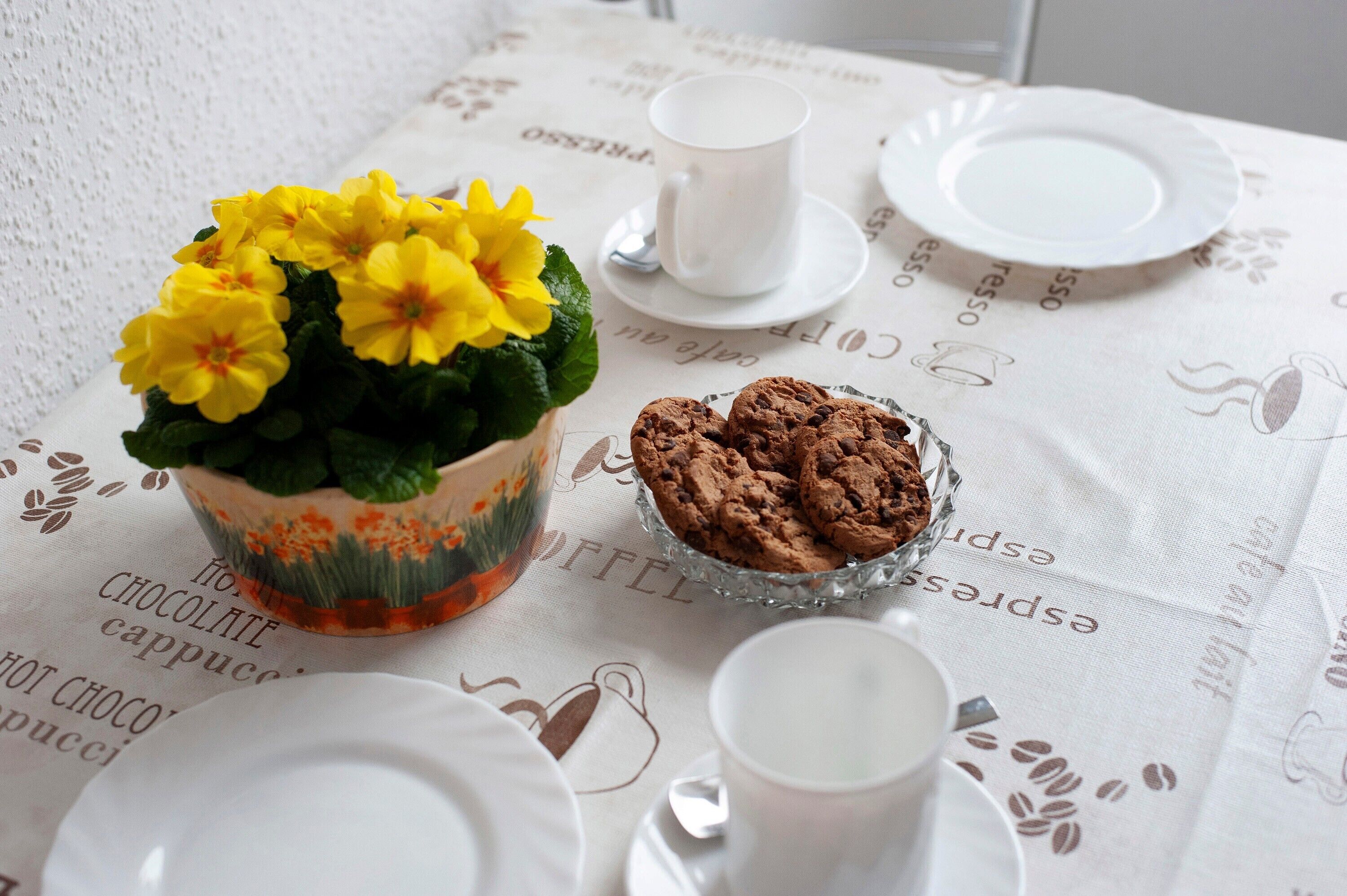 A table with a coffee cup, a plate with cookies, and a flower arrangement.