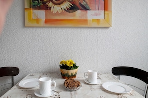 A dining table with a floral tablecloth, a coffee cup, a plate, a cookie, and a flower vase. - Holiday Apartment 'Laage' with Wi-Fi (Laage)