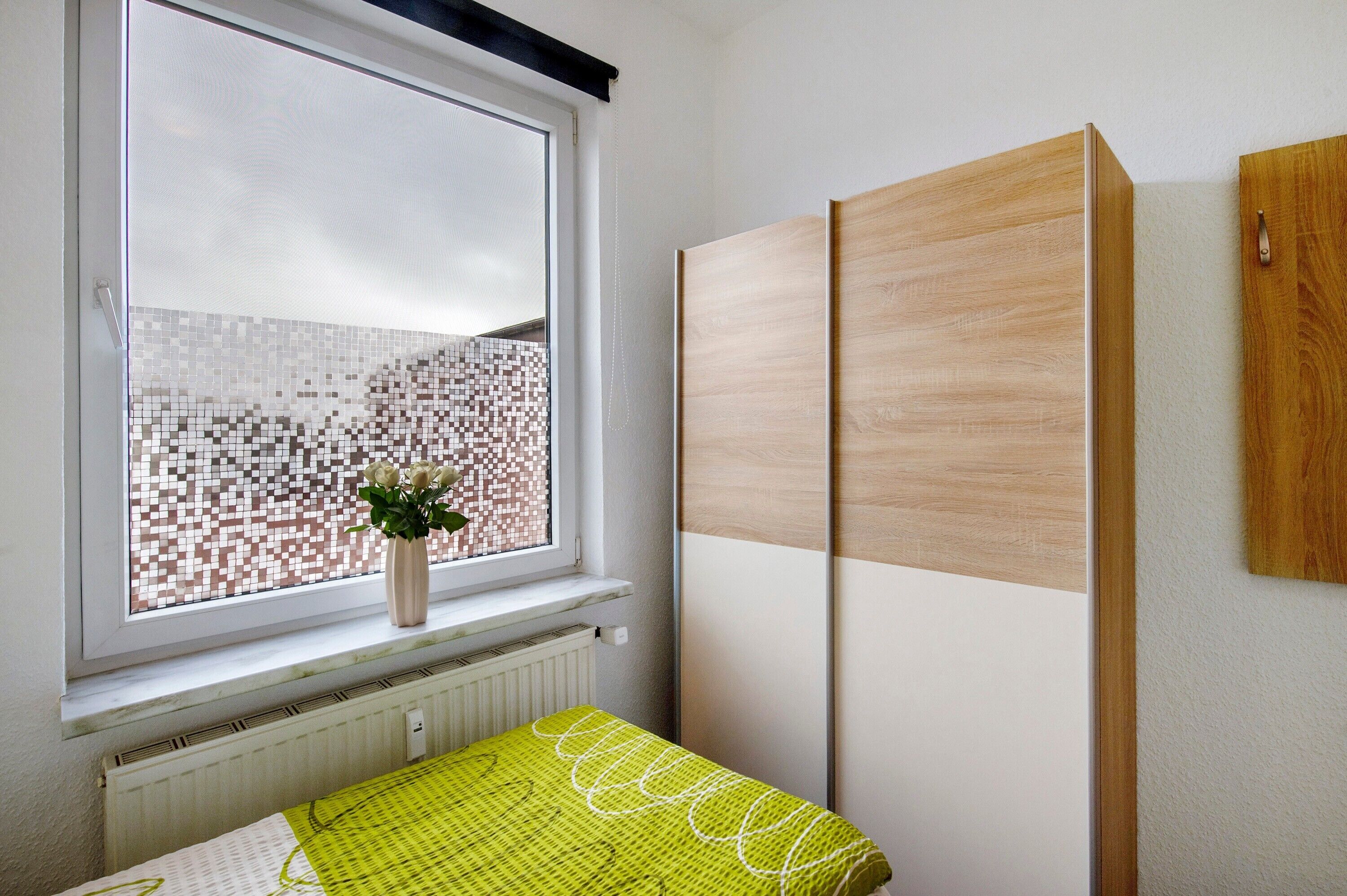 A room with a window, a radiator, a bed with a green bedspread, and a wooden wardrobe.