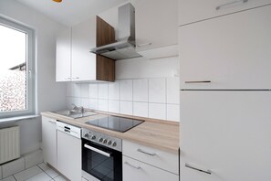 A modern kitchen with white cabinets, a black oven, a stainless steel range hood, and a window with a view. - Holiday Apartment 'Laage' with Wi-Fi (Laage)