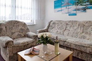 A living room with a sofa, armchair, a vase with flowers, a bottle, and a magazine on a table. - Holiday Apartment 'Laage' with Wi-Fi (Laage)
