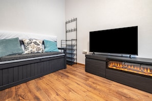 A modern living room with a sofa, a mounted TV, a fireplace, and a wall-mounted coat rack.