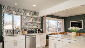 A modern kitchen with white cabinetry, a built-in dishwasher, and a coffee station. - Modern Oasis – 6BR Arvada Retreat, Sleeps 14, Hot Tub, Walkable to Olde Town (Arvada)
