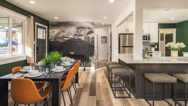 A modern kitchen with a large island, wooden flooring, and a dining area with a mountain mural. - Modern Oasis – 6BR Arvada Retreat, Sleeps 14, Hot Tub, Walkable to Olde Town (Arvada)