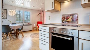 A modern kitchen with white cabinets, a built-in oven, and a dining area with a table and chairs. - Apartment 'Kropp' with Private Terrace, Private Garden and Wi-Fi (Knorrendorf)