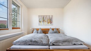 A bedroom with a wooden bed, grey bedding, a window, and a sailboat painting on the wall. - Apartment 'Kropp' with Private Terrace, Private Garden and Wi-Fi (Knorrendorf)