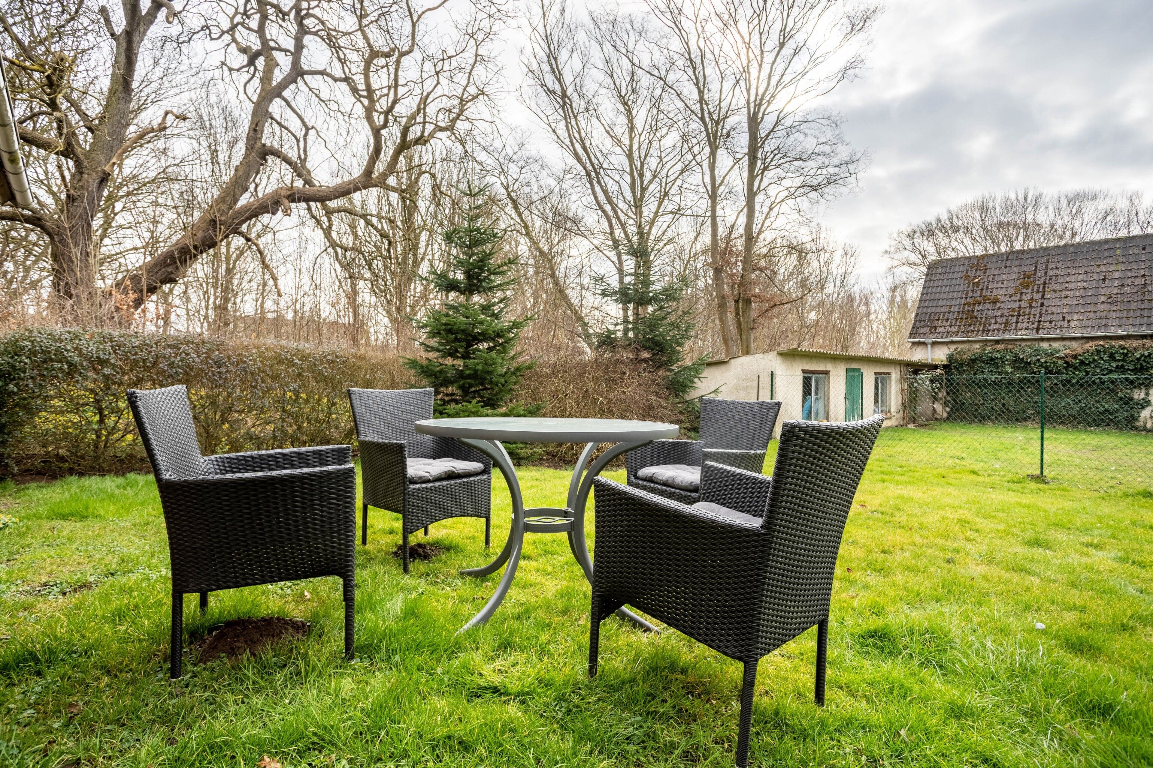 An outdoor patio with wicker furniture, a round table, and a view of a house in the background.