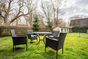 Eine Terrasse im Freien mit Korbmöbeln, einem runden Tisch und Blick auf ein Haus im Hintergrund.