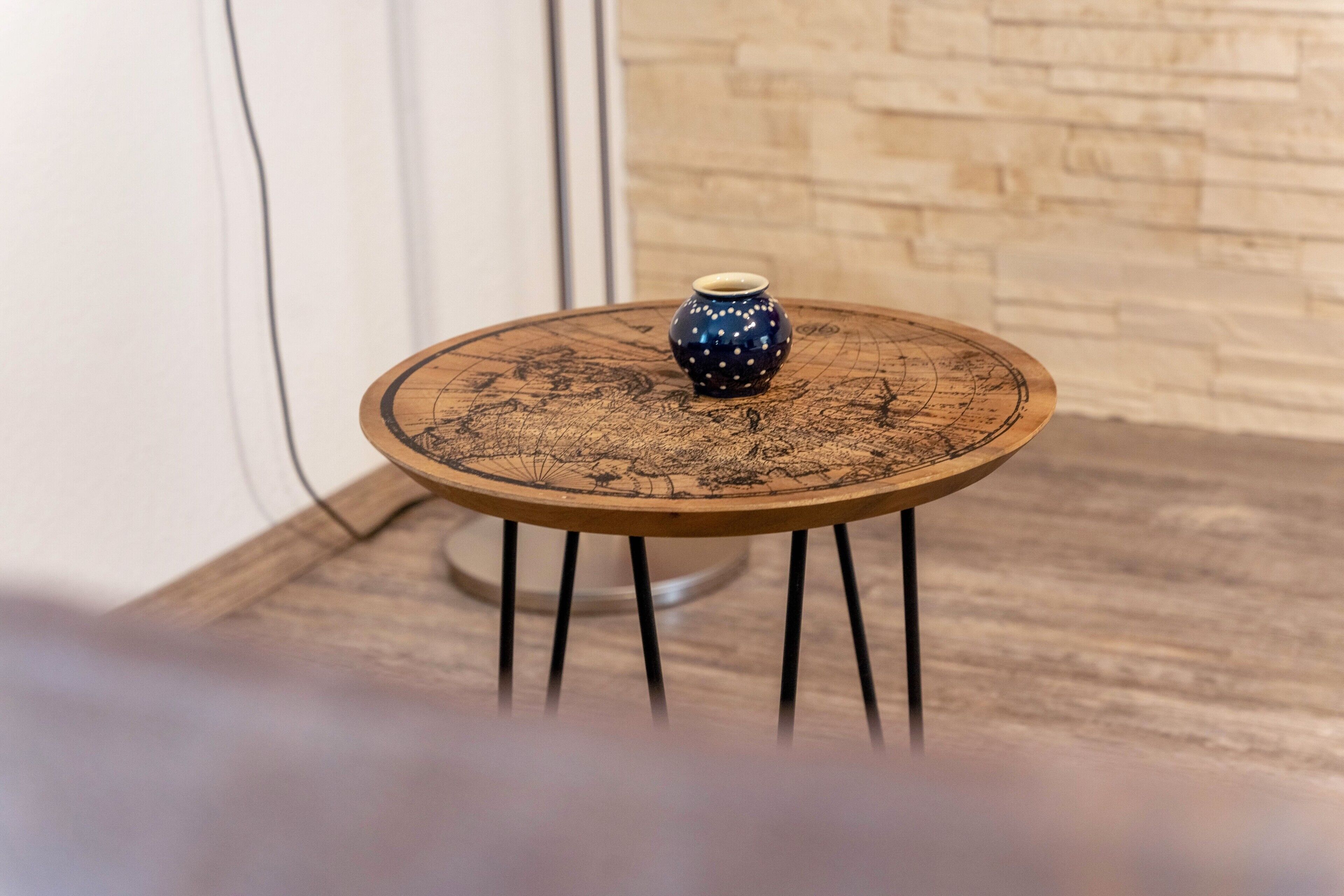 A small round table with a decorative vase on top, set against a brick wall.