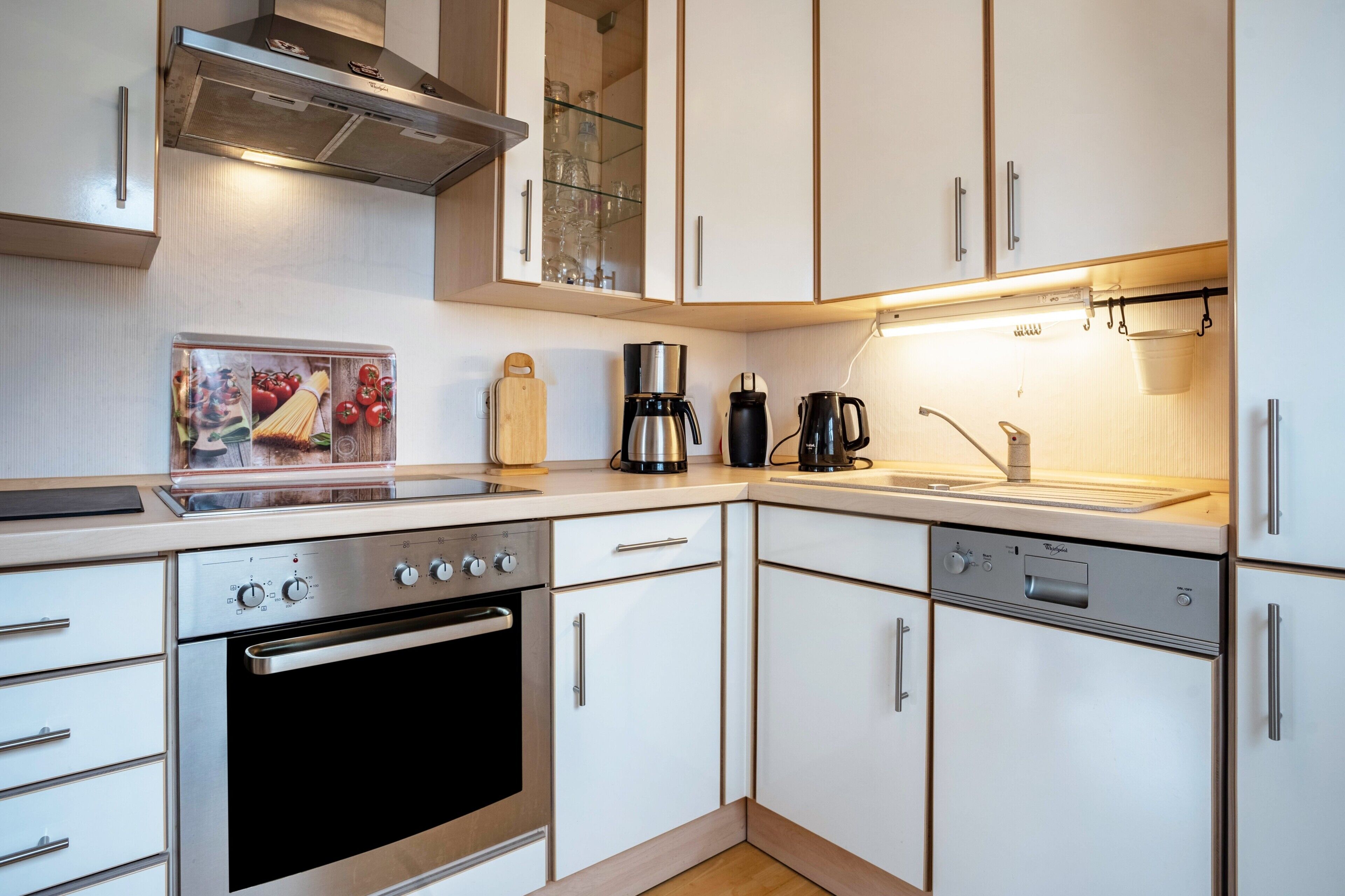 Une cuisine moderne dotée d’appareils électroménagers en acier inoxydable, de meubles blancs et d’un four encastré.