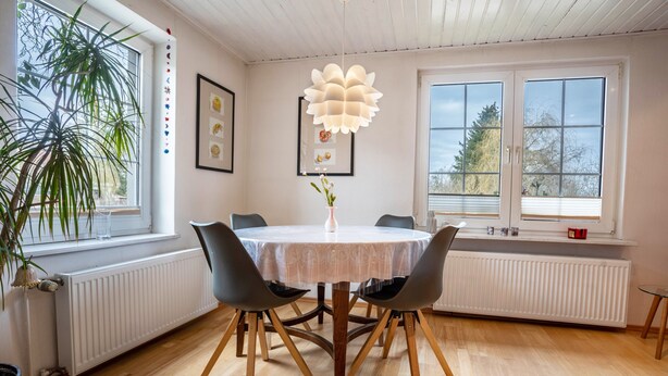 A dining area with a round table, four chairs, a hanging light fixture, a potted plant, and a window with a view of trees. - Apartment 'Kropp' with Private Terrace, Private Garden and Wi-Fi (Knorrendorf)
