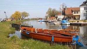 Un bote de madera amarrado en un río tranquilo, con una pequeña casa y un muelle al fondo.