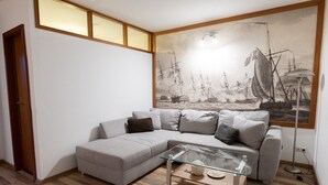Una sala de estar con un sofá gris, una mesa de centro de vidrio y un cuadro grande con temática marina en la pared.
