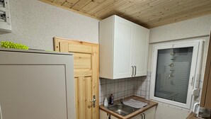 Eine kleine Küche mit Holzboden, weißen Schränken, einem Fenster und einem eingebauten Herd.