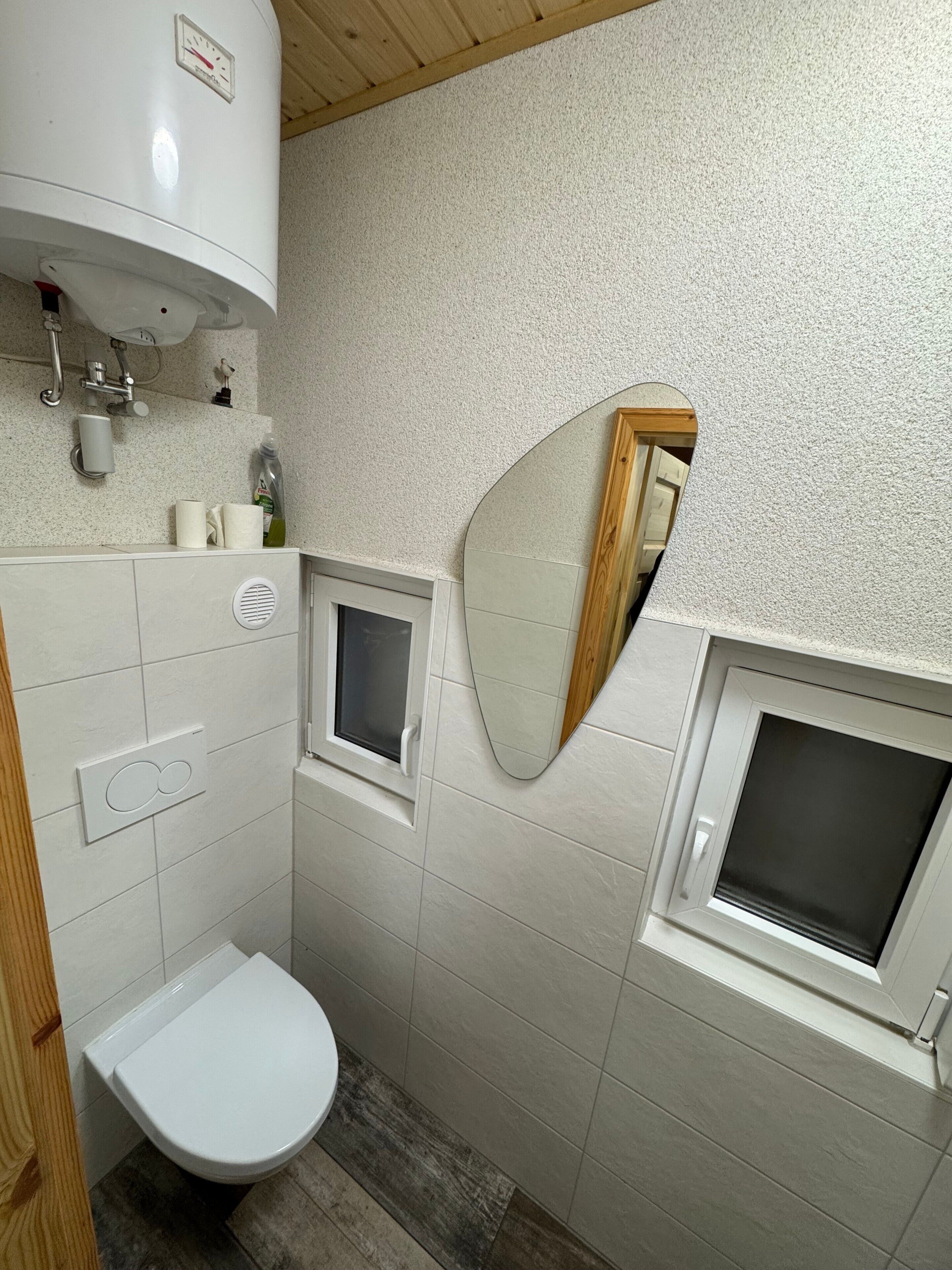 Un baño con inodoro, espejo, ventana y zona de ducha.