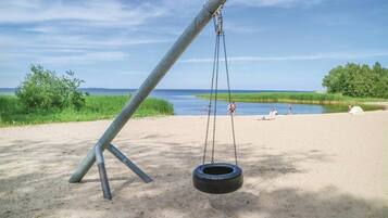 A swing set with a tire swing, a sandy beach, and a body of water in the background.