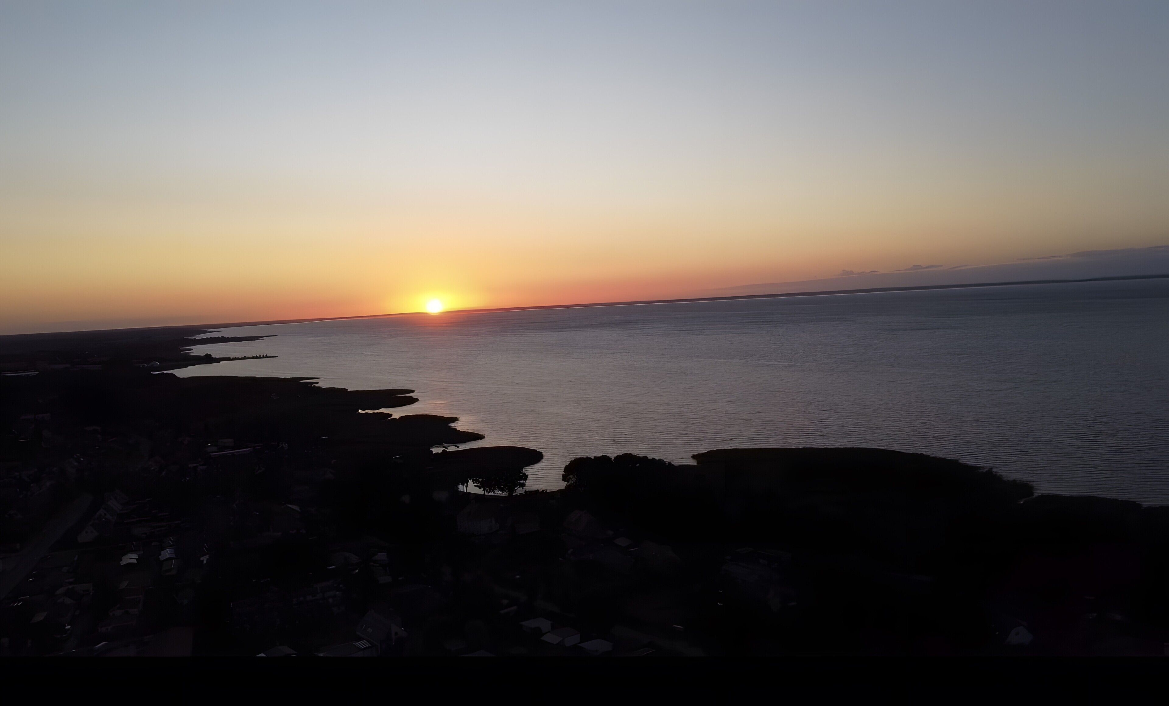 A coastal sunset with a calm sea and rocky shoreline.