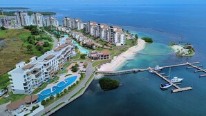 A coastal resort with multiple high-rise buildings, a central swimming pool, a beach, and a marina with boats. - 4-bedroom apartment Ocean & Marina View, in Playa Escondida Marina & Resort (Maria Chiquita)