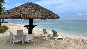 A beach with a thatched umbrella, white lounge chairs, and a sandy shoreline. - 4-bedroom apartment Ocean & Marina View, in Playa Escondida Marina & Resort (Maria Chiquita)
