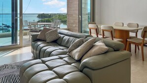 Un salon moderne avec un canapé en cuir, une table à manger avec des chaises et de grandes portes vitrées donnant sur un balcon avec vue sur la mer.