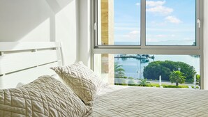 A bedroom with a large window offering a view of a marina and greenery. - 4-bedroom apartment Ocean & Marina View, in Playa Escondida Marina & Resort (Maria Chiquita)