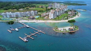Une vue aérienne d’un complexe hôtelier comprenant plusieurs bâtiments, un port de plaisance et une petite île dotée d’une plage et d’une construction.