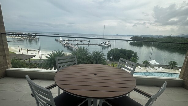 A round table with four chairs on a balcony overlooking a marina with boats and a beach. - 4-bedroom apartment Ocean & Marina View, in Playa Escondida Marina & Resort (Maria Chiquita)